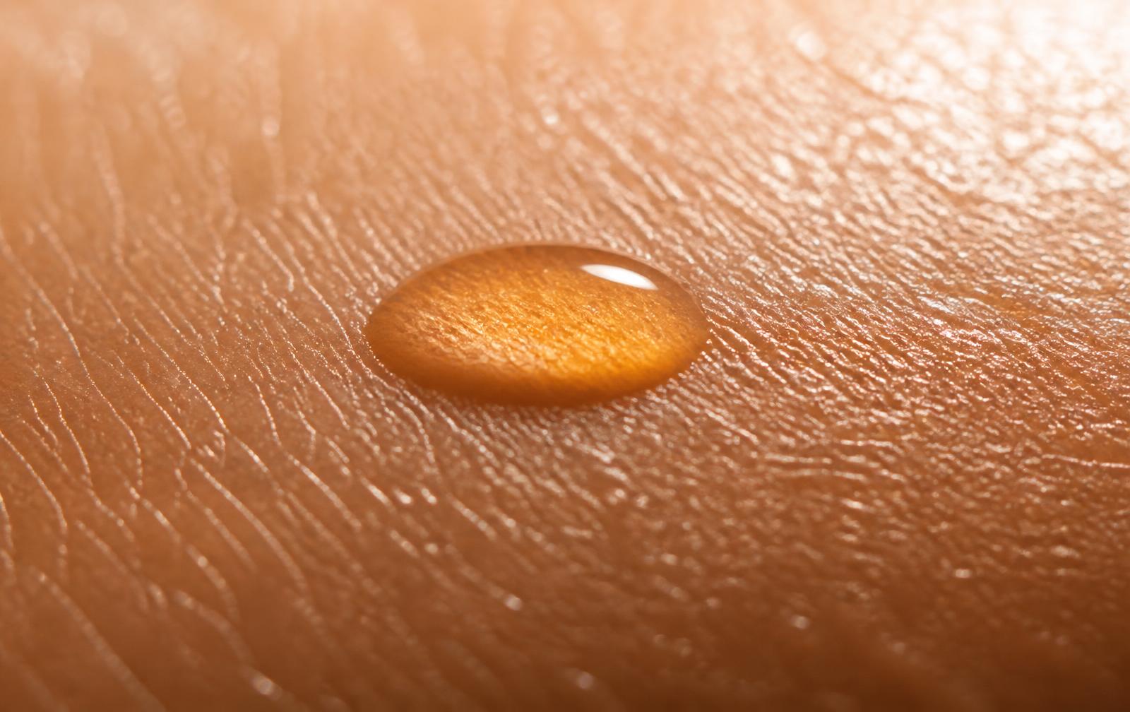 Macro d'une goutte d'huile dorée sur la peau